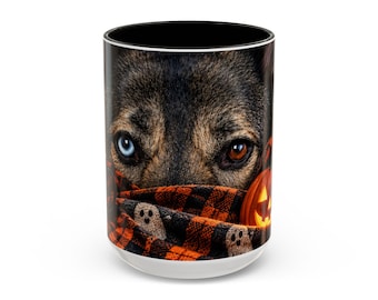 Op de afbeelding: Een cilindervormige keramische mok met een fotoprint van een hond met één blauw en één bruin oog. De hond is gewikkeld in een oranje en zwarte sjaal met een ruitpatroon en kleine witte spookjes, naast een gloeiende oranje pompoen.