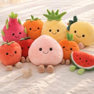 Puede incluir: Una colección de juguetes de peluche con forma de frutas, incluyendo una pitahaya rosa, un tomate naranja, una piña amarilla y una rodaja de sandía. Cada juguete tiene una cara sonriente y pequeñas piernas.