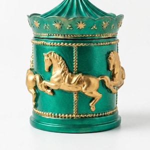 May include: An emerald green carousel-themed container with gold detailing. The container features gold carousel horses and star details. The lid is shaped like a circus tent. A decorative accent piece.