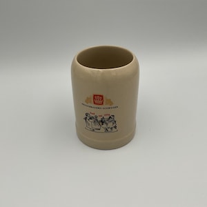 May include: A beige ceramic beer mug featuring a red and white crown logo above the text PRIVATBRAUEREI SCHWEIGER. Below the text is a black and white illustration of two figures holding mugs with the red text Fest und fittig printed above them.