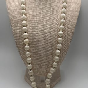 May include: A long necklace featuring a single strand of round, off-white satin-finish beads. Each bead is separated by a small, polished silver-tone metal spacer bead, creating a consistent pattern throughout the entire length of the jewelry piece.