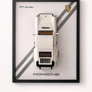 Peut inclure: Une œuvre encadrée représentant une Porsche 911 Turbo blanche en Lego. La voiture est placée sur un fond blanc avec des rayures diagonales grises. Le logo Porsche et le texte "911 Turbo" sont visibles.