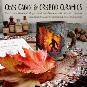 Könnte beinhalten: Eine handgefertigte Steinzeugtasse mit einem Baumrinden-Design und einer Waldszene mit einer Bigfoot-Silhouette. Die Tasse ist Teil der Cozy Cabin & Cryptid Ceramics-Kollektion. Das Bild enthält auch ein Buch, Herbstblätter und kleine Flaschen.