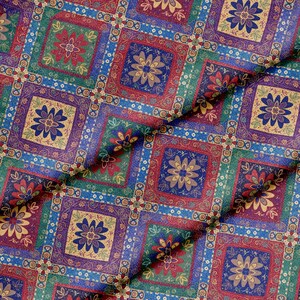 Op de afbeelding: Een geweven stof met een herhalend rasterpatroon van vierkanten. Elk vierkant bevat een gestileerd bloemmotief in tinten rood, blauw, groen en goud. Het ontwerp bevat ingewikkelde decoratieve randen rond elke bloem, wat zorgt voor een dicht, kleurrijk en getextureerd textieloppervlak met een zichtbare weefstructuur door het gehele materiaal.