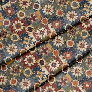 Puede incluir: Una tela con un patrón de patchwork repetitivo de estrellas de múltiples puntas en tonos azul marino, rojo intenso, verde oliva y amarillo mostaza. El diseño consta de bloques cuadrados dispuestos en cuadrícula, creando un motivo geométrico denso.