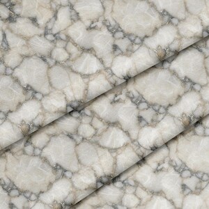Puede incluir: Una pieza de tela doblada con un patrón repetitivo que imita la apariencia de piedra natural o mármol. El diseño consiste en formas irregulares y redondeadas de color blanco roto y beige, delineadas por vetas finas de color gris oscuro.