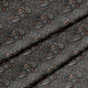 Op de afbeelding: Een donkergrijze stof met een herhalend patroon van motorfietsen en schedels. Het ontwerp bevat ingewikkelde krulwerk- en filigraandetails in koper- en bronskleuren, wat een dicht, gestructureerd visueel effect over het hele oppervlak creëert.