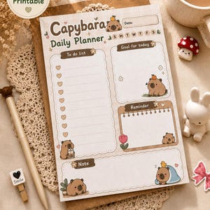 Puede incluir: Una hoja de planificador diario imprimible en tamaño A5 con ilustraciones de capibaras, una lista de tareas con casillas de verificación en forma de corazón, una sección de objetivos, un cuadro de recordatorios y notas con el texto Capybara Daily Planner.