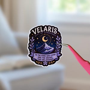 Puede incluir: Una pegatina troquelada con un paisaje montañoso en tonos morados y azul oscuro bajo una luna creciente y un cielo estrellado. El texto dice Velaris City of Starlight y To the stars who listen and the dreams that are answered, enmarcado por hojas.