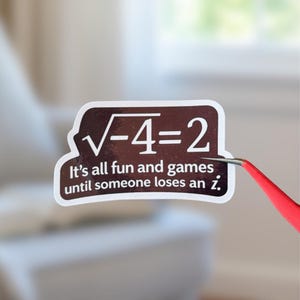May include: A white sticker with a brown border and the text "√-4=2 It's all fun and games until someone loses an i." is held by red tweezers. The sticker has a math theme.