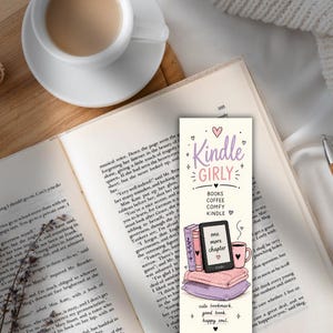 以下が含まれることがあります： クリーム色の背景に紫とピンクの文字でKindle Girly, Books, Coffee, Comfy, Kindleと書かれた長方形のしおり。積み重ねられた本、one more chapterと表示された黒い電子書籍リーダー、ピンクのマグカップのイラストが描かれています。
