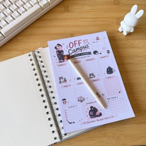 May include: A light purple weekly planner sheet titled OFF CAMPUS with sections for each day of the week, a to-do list, a habit tracker, and illustrations of a couple, cats, a backpack, and books. A white pen with a brown bear topper rests on the planner.