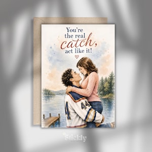 May include: A greeting card featuring a watercolor illustration of a person in a white and blue jersey holding another person in a pink sweater. The text reads, You're the real catch, act like it! with a small heart icon above a lake and forest.
