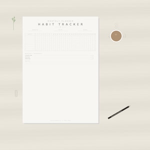 Op de afbeelding: Een minimalistische maandelijkse habit tracker op crèmekleurig papier, met de titel "HABIT TRACKER". Een kopje koffie en een potlood liggen op een licht oppervlak met houtnerf. Een kleine groene plant en een paperclip zijn ook zichtbaar.