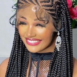 Puede incluir: Una mujer con una peluca trenzada con un patrón en zigzag en la coronilla y trenzas largas y gruesas. Lleva un top negro con una superposición de red de pesca y un adorno brillante. La mujer también lleva pendientes colgantes.