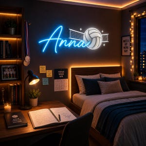 May include: A custom neon wall sign featuring the name Anna in blue script lettering, accompanied by a white glowing volleyball and a net graphic. The sign is mounted on a dark wall above a bed in a bedroom setting with warm ambient lighting.