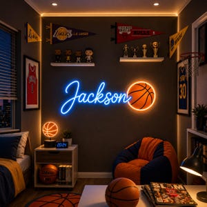 May include: A room featuring a blue neon sign reading Jackson next to an orange basketball neon light. The wall displays sports pennants, framed jerseys, and shelves with figurines and trophies. A beanbag chair, basketballs, and a lamp are present.