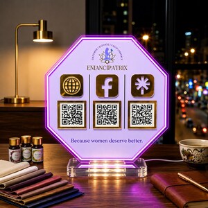 May include: An octagonal light-up sign with a purple border and a light purple face. It features the text ENIANCIPATRIX, a logo, three gold social media icons, three QR codes, and the text Because women deserve better. It sits on a clear base.