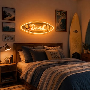 Puede incluir: Un dormitorio con temática de surf. Un letrero de neón con forma de tabla de surf con el nombre "Daniel's" está montado sobre una cama con ropa de cama azul y gris. Tablas de surf y arte temático de surf decoran las paredes.