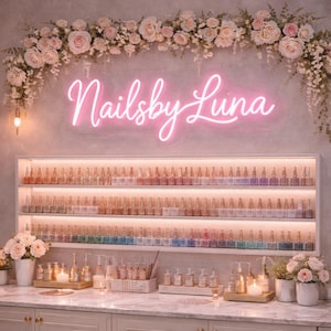Könnte beinhalten: Innenansicht eines Nagelstudios mit einem Neon-Schild "Nailsby Luna". Die Wände sind mit Blumenschmuck verziert, und Regale präsentieren eine große Auswahl an Nagellackfarben. Die Gesamtästhetik ist sanft und feminin.