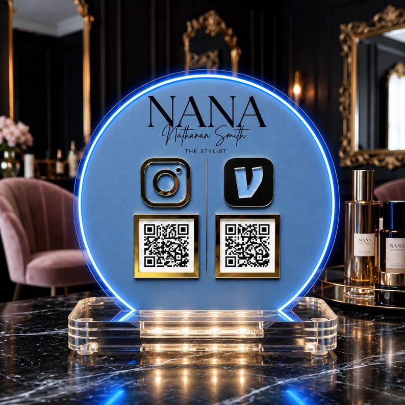 May include: A circular blue acrylic sign with a glowing neon blue border, featuring the text NANA NATHANAN SMITH THE STYLIST, Instagram and Vimeo icons, and two square QR codes. The sign is mounted on a clear rectangular acrylic base.