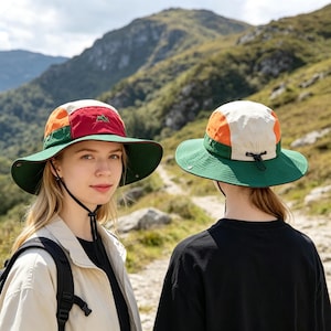 Peut inclure: Deux chapeaux de plein air à larges bords. L'un a un bord vert, un dessus rouge et blanc avec un logo de montagne et un panneau latéral orange. L'autre a un bord vert, un dessus orange et blanc et un cordon de serrage noir. Les deux chapeaux sont portés sur un sentier de montagne.