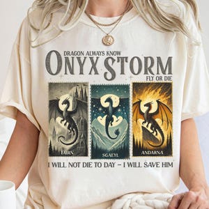K&ouml;nnte beinhalten: Cremefarbenes T-Shirt mit einem Drachen-Design. Das Shirt zeigt den Text "DRAGON ALWAYS KNOW ONYX STORM FLY OR DIE" &uuml;ber drei Drachenillustrationen. Unter den Illustrationen steht "TAIRN", "SGAEYL" und "ANDARNA". Der Text unten lautet "I WILL NOT DIE TO DAY - I WILL SAVE HIM".