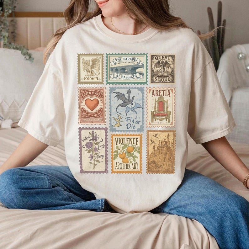 May include: A cream-coloured t-shirt displaying nine postage stamp-style graphics. The stamps feature illustrations like a dragon, a heart, and text including "Fly or Die" and "Violence Apothecary".