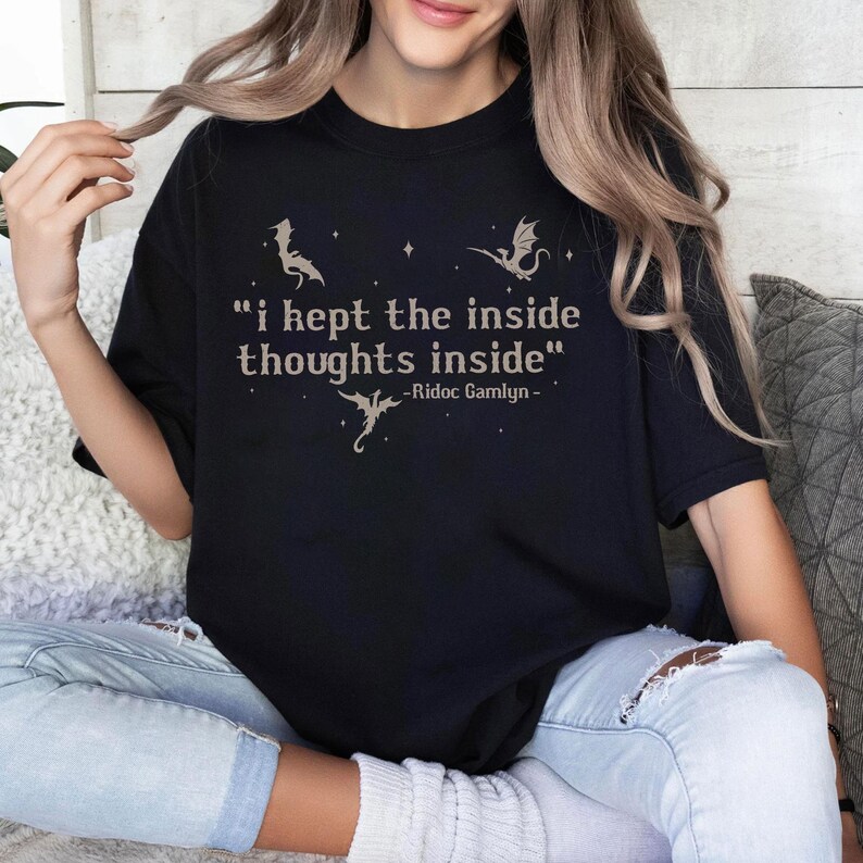 May include: Black t-shirt with the quote "i kept the inside thoughts inside" and dragon illustrations. The quote is in a serif font, with the author's name, Ridoc Gamlyn, below. The shirt is a comfortable, casual style.
