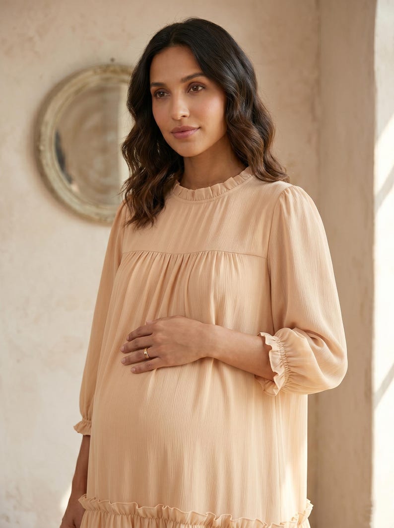 May include: A light beige long-sleeved dress featuring a ruffled high neckline, gathered bodice, and ruffled cuffs. The fabric has a subtle vertical texture, and the garment includes a tiered skirt design with a ruffled hemline detail.