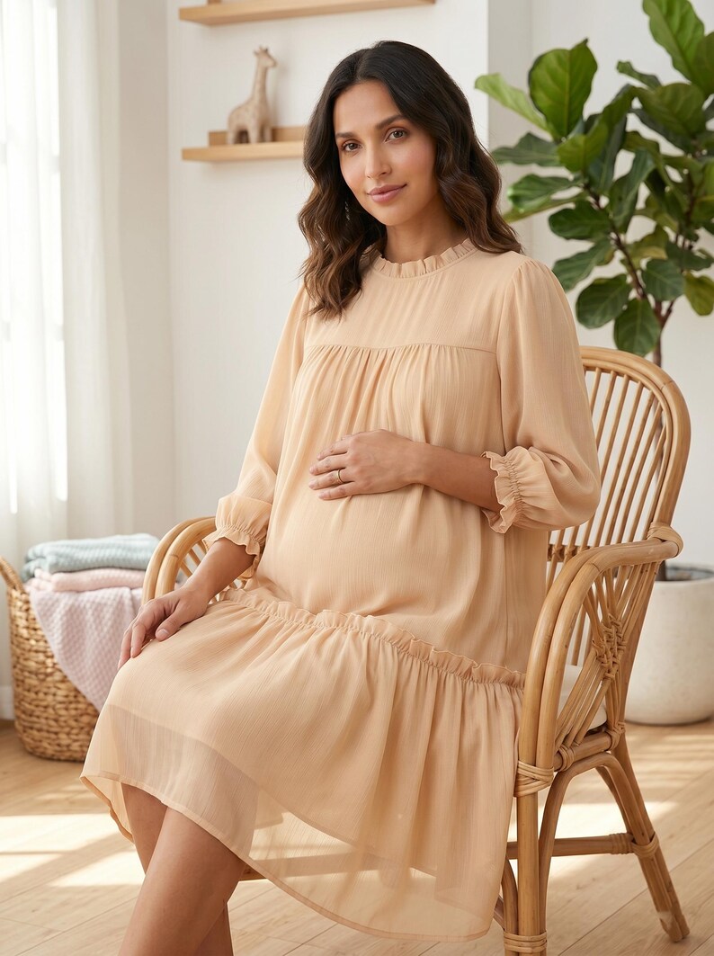 May include: A knee-length, light beige dress with long sleeves, a ruffled mock neckline, and a gathered drop-waist skirt. The dress features sheer, lightweight fabric with a subtle texture, ruffled sleeve cuffs, and a loose, flowing silhouette.