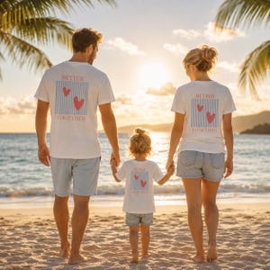 Könnte beinhalten: Eine dreiköpfige Familie geht am Strand spazieren, bekleidet mit passenden weißen T-Shirts mit den Worten "Better Together" und Herzgrafiken. Der Himmel ist golden und Palmen umrahmen die Szene.