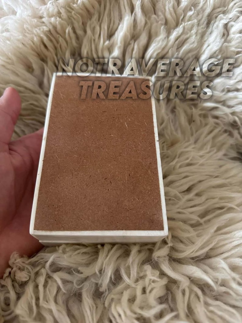 May include: A rectangular box with a smooth white border and a flat, textured brown center panel. The text NOTAVERAGE TREASURES is printed in a bold, sans-serif font across the top portion of the object, which has a clean, geometric design.