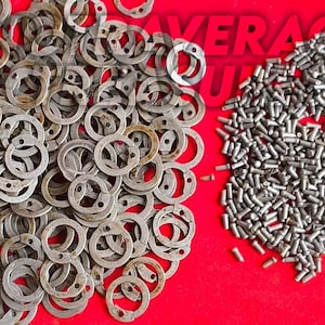 May include: A red surface displays two distinct piles of metal hardware. One pile consists of numerous circular retaining rings with holes, while the other is a collection of small, cylindrical metal fasteners. The word "AVERAGE" is partially visible.