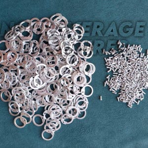 May include: A collection of silver metal washers and small screws are arranged on a teal surface. The washers are circular with a small hole and a tab. The text "AVERAGE STORE" is visible in the background.