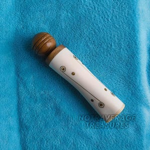 May include: A decorative bottle stopper with a wooden top and a white body. The white body is decorated with gold-coloured circular and dot designs. The text "NOTAVERAGE TREASURES" is visible on the bottom.