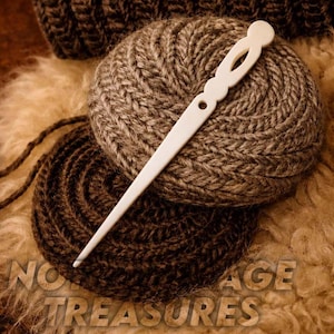 May include: A white bone knitting needle lies across two balls of yarn in shades of brown and beige. The yarn is tightly wound, and the needle has a decorative top with an oval cutout. The image has the text "NO AGE TREASURES" at the bottom.
