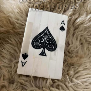 May include: A rectangular decorative plaque designed as an ace of spades playing card. The surface is composed of vertical off-white bone-like segments with a large, intricate black spade symbol in the center and the letter A in the corners.