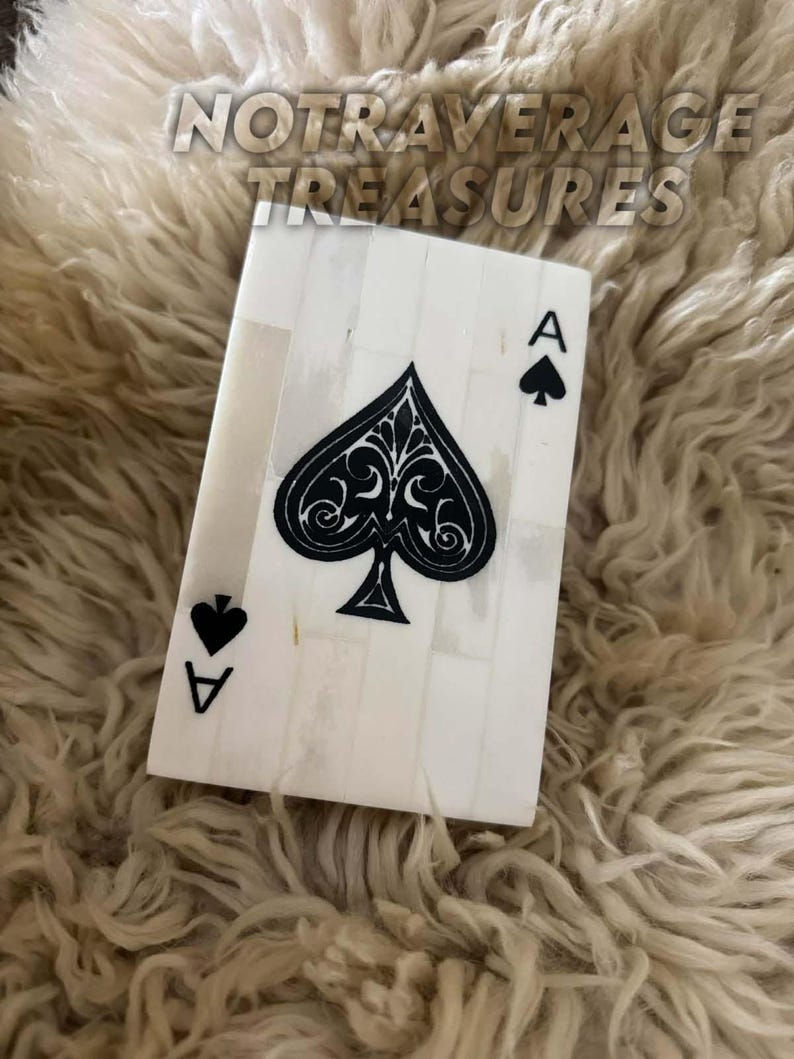 May include: A rectangular decorative plaque designed as an ace of spades playing card. The surface is composed of vertical off-white bone-like segments with a large, intricate black spade symbol in the center and the letter A in the corners.