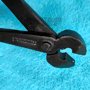 Könnte beinhalten: Schwarze Metallkneifzange mit grünen Griffen. Das Werkzeug hat eine gebogene Schneide und das Wort "KLEINTOOLS" ist auf der Seite eingeprägt. Die Kneifzange befindet sich vor einem strukturierten blauen Hintergrund.