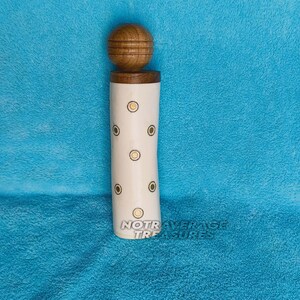 May include: A decorative bottle stopper with a wooden ball top and a cream-coloured body. The body features six circular designs with yellow and brown accents. The text "NOT AVERAGE TREASURES" is visible on the bottom.
