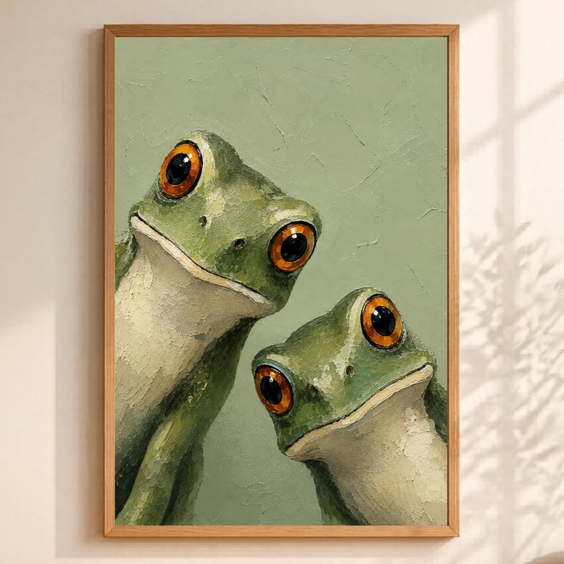 May include: A framed art print featuring two green frogs with large, orange eyes. The frogs are painted with a textured, oil-paint style against a muted green background. The artwork is encased in a natural wood frame.