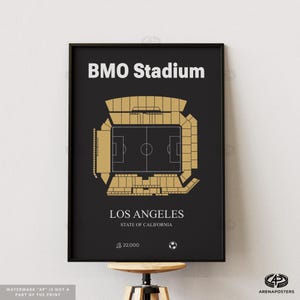May include: Framed black poster featuring a gold and black stadium layout. The text "BMO Stadium" is at the top, with "LOS ANGELES, STATE OF CALIFORNIA" below. The poster includes a capacity of 22,000 and a soccer ball icon.