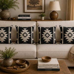 May include: Four square throw pillows featuring a black and beige geometric pattern. Each pillow displays a central diamond motif surrounded by stepped triangular shapes, creating a symmetrical design on a textured fabric surface.
