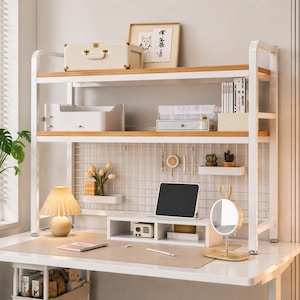 Könnte beinhalten: Ein weißer und holzfarbener Schreibtisch-Organizer mit mehreren Regalen, einer Schreibtischlampe und einem Tablet. Das oberste Regal enthält einen kleinen Koffer und gerahmte Kunstwerke. Der Schreibtisch hat eine Gitterrückwand und einen kleinen Spiegel.