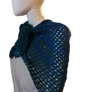 May include: A dark blue and forest green crochet shawl featuring an open, airy lattice stitch pattern. The garment is draped over the shoulders and fastens at the front with a matching crocheted tie, creating a textured, layered appearance.