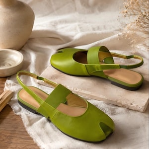 May include: A pair of lime green flat slingback shoes featuring a split-toe design, a wide strap across the instep, and a thin adjustable heel strap. The shoes have a smooth finish, a low black sole, and a rounded silhouette with a front toe opening.