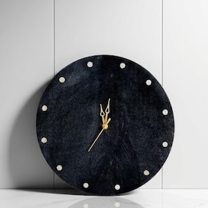 Könnte beinhalten: Eine runde, schwarze Wanduhr mit goldfarbenen Zeigern und Stundenmarkierungen. Das Zifferblatt hat eine strukturierte Oberfläche, und die Stundenmarkierungen sind kleine, weiße Punkte. Ein dekorativer Artikel für die Inneneinrichtung.