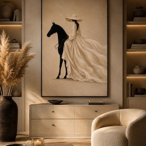 May include: A framed wall art print featuring a silhouette of a black horse and a figure wearing a wide-brimmed hat and a long, flowing cream-colored dress. The artwork is set against a neutral beige background, capturing a contrast between the dark horse and the light, voluminous fabric of the garment.