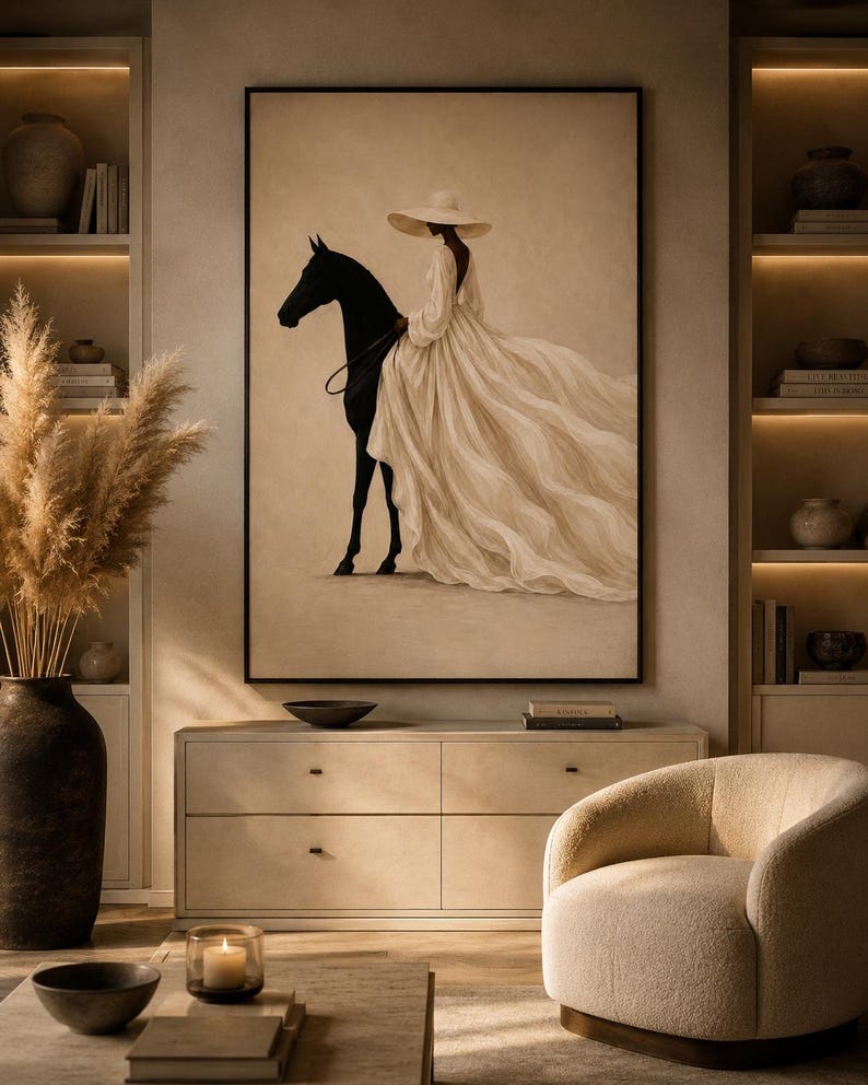 May include: A framed wall art print featuring a silhouette of a black horse and a figure wearing a wide-brimmed hat and a long, flowing cream-colored dress. The artwork is set against a neutral beige background, capturing a contrast between the dark horse and the light, voluminous fabric of the garment.